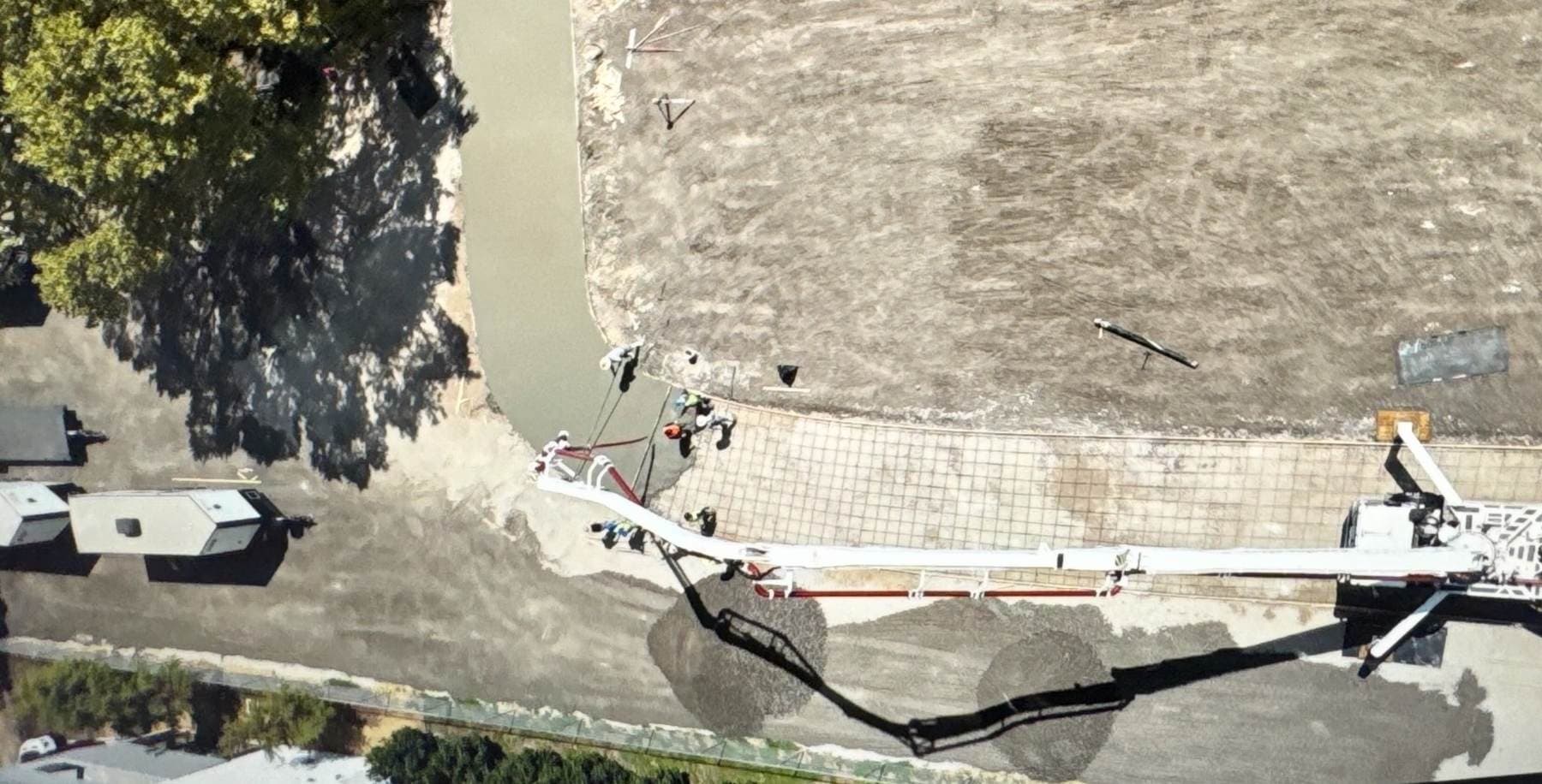 Aerial view of a concrete pump boom placing concrete over a rebar mat while a crew screeds the slab edge